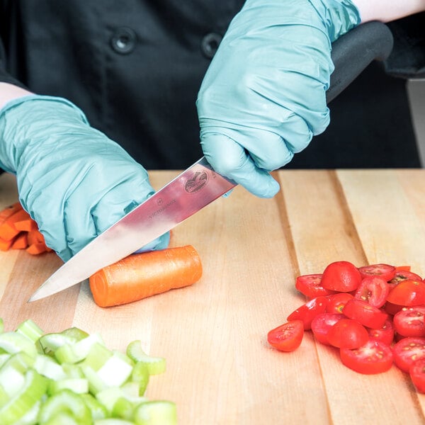 A person in blue gloves using a Victorinox Chef Knife to cut vegetables on a cutting board.