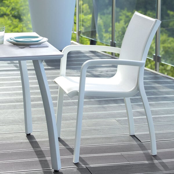 A white Grosfillex Sunset resin arm chair on a wooden deck.