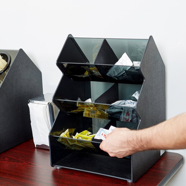 A man using a Vollrath 3 tier condiment holder to store condiment packets on a hotel buffet counter.