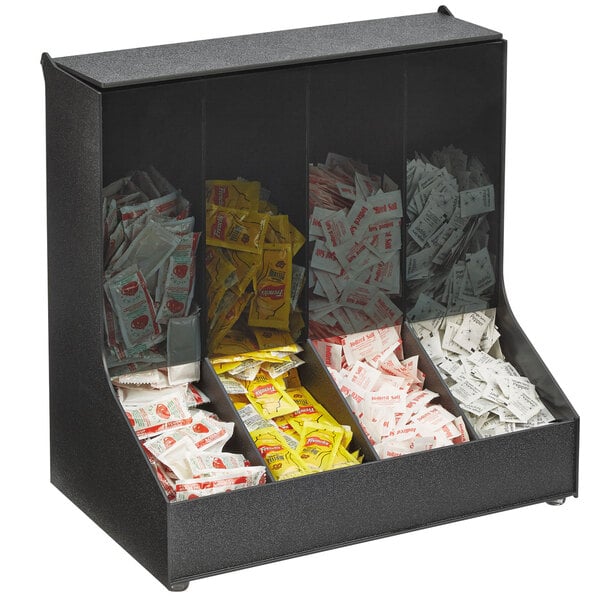 A black Vollrath first in first out gravity fed condiment holder on a counter filled with condiment packets.