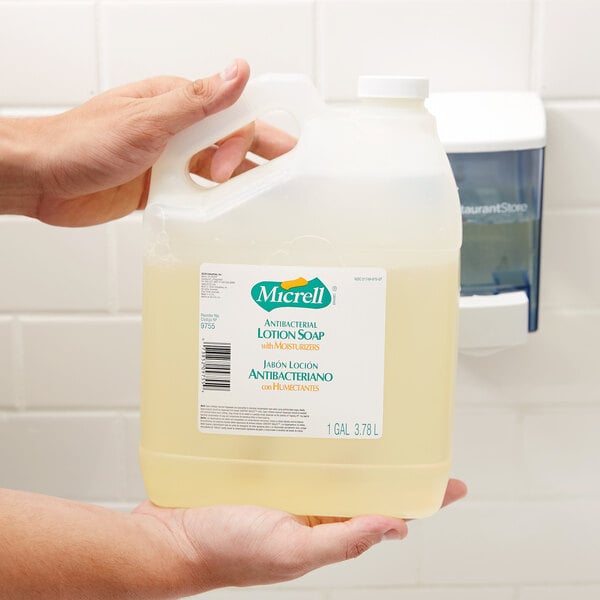A hand holding a jug of Micrell floral antibacterial lotion hand soap.