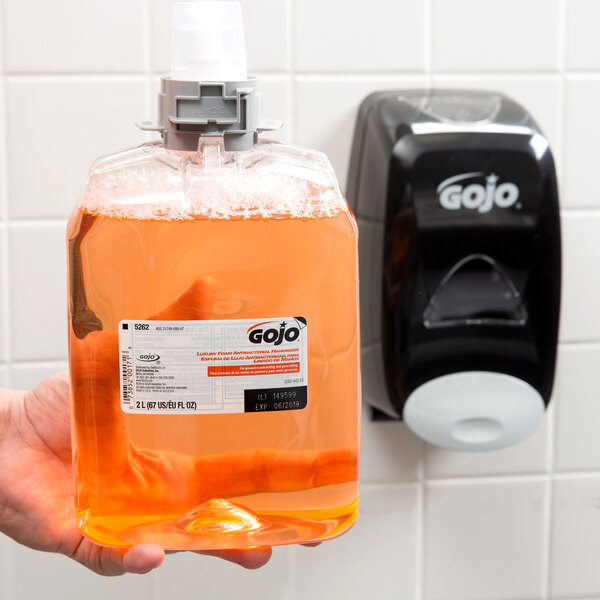 A hand holding a plastic bottle of GOJO Luxury Orange Blossom foaming antibacterial hand soap.