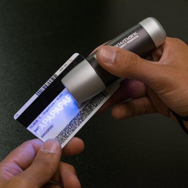 A person holding a credit card with a Dri Mark UV PRO counterfeit detector light.