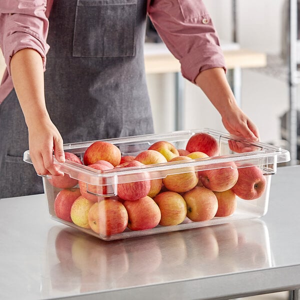A woman holding a Cambro clear polycarbonate food storage box filled with apples.