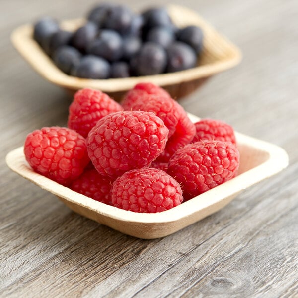 A table with bowls of raspberries and blueberries in EcoChoice palm leaf bowls.