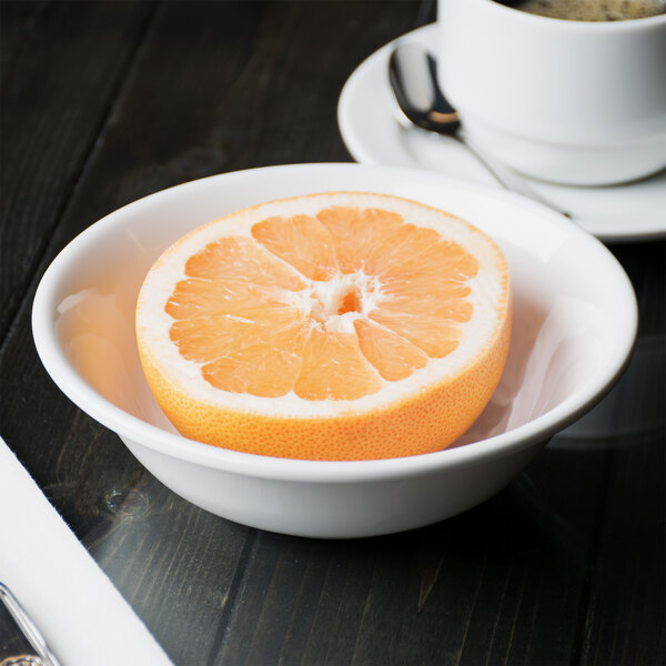A Libbey aluma white porcelain grapefruit bowl with half a grapefruit in it next to a cup of coffee.
