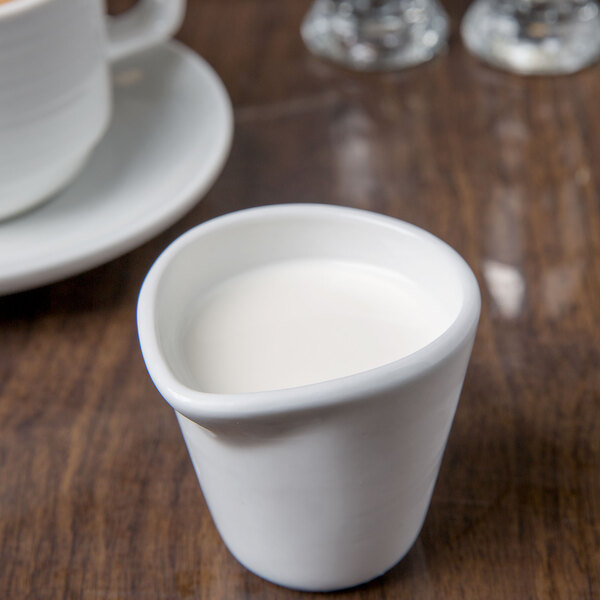 A white Libbey porcelain creamer filled with white liquid on a table.