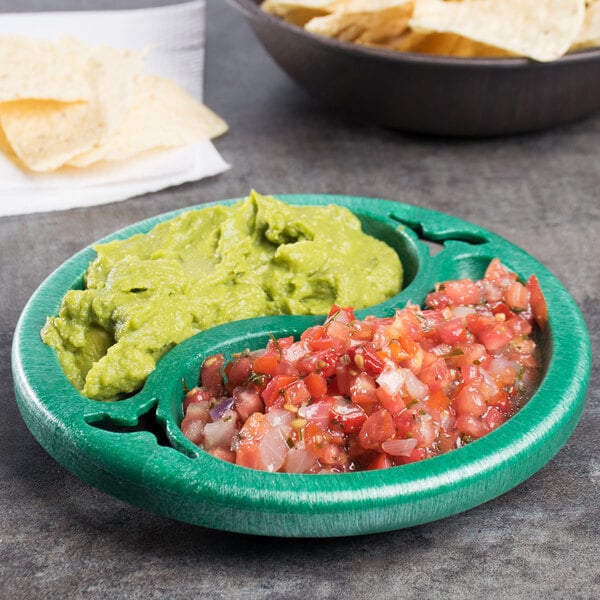 A green divided plastic bowl with guacamole and chips on a table.