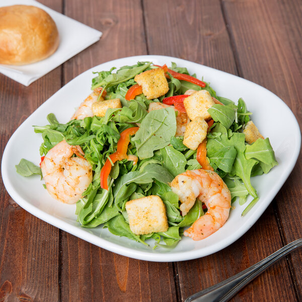 A plate of salad with shrimp, greens, and vegetables on a Libbey Aluma White Porcelain square coupe plate.