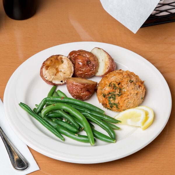 A Libbey ivory porcelain plate with food including a meatball, green beans, and potatoes.