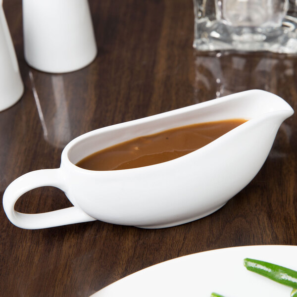 A white Libbey porcelain gravy boat filled with brown sauce on a table.
