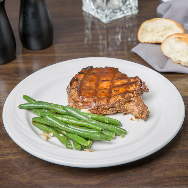 A Libbey ivory porcelain plate with steak and green beans on it.