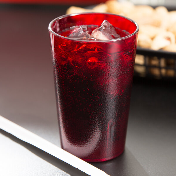 A Cambro ruby red plastic tumbler filled with red liquid and ice with a straw.
