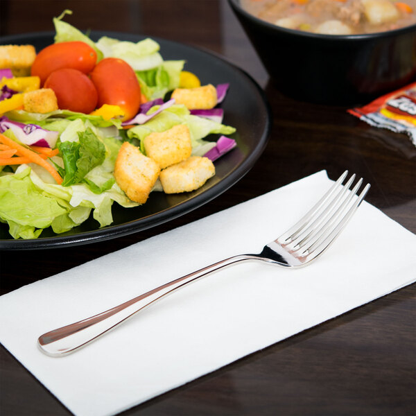 A Libbey stainless steel dessert fork on a plate of salad with croutons and tomatoes.