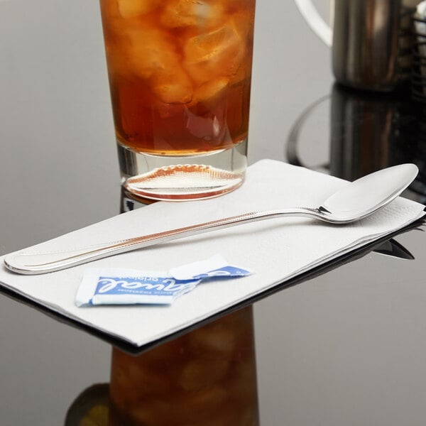 A glass of iced tea with a Libbey stainless steel iced tea spoon on a napkin.