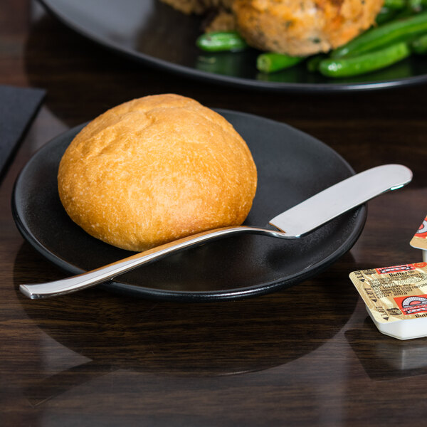 A plate with a roll and a Libbey stainless steel butter spreader on it.