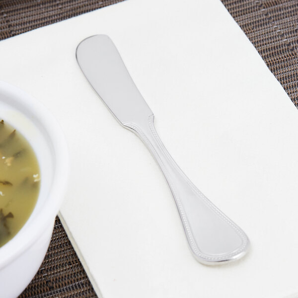 A Libbey stainless steel butter spreader on a napkin next to a bowl of soup.
