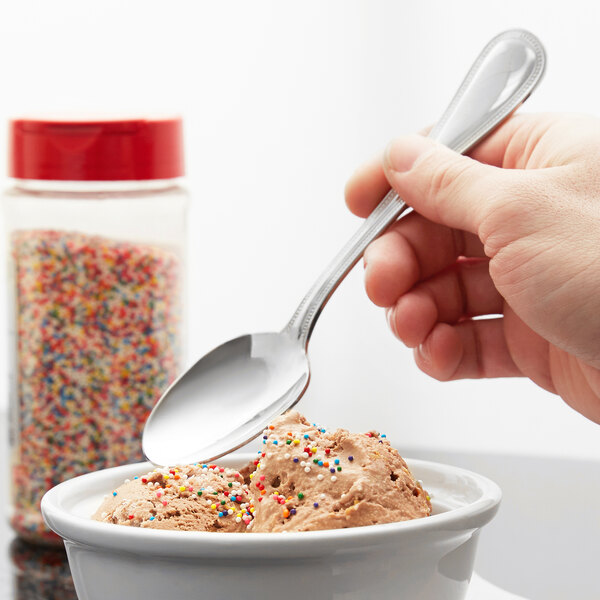 A hand using a Libbey stainless steel dessert spoon to scoop sprinkles onto a bowl of ice cream.