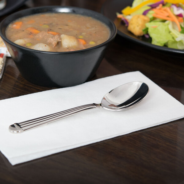 A bowl of soup and a Libbey stainless steel bouillon spoon on a napkin.
