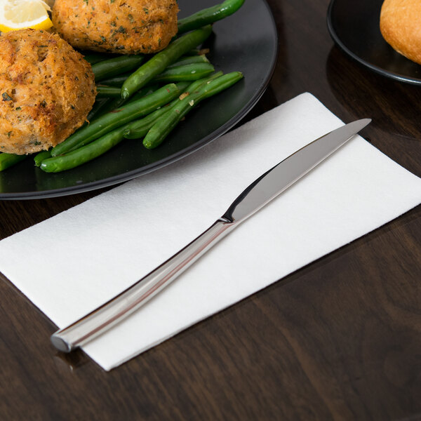 A Libbey stainless steel dinner knife on a napkin next to a plate of food.