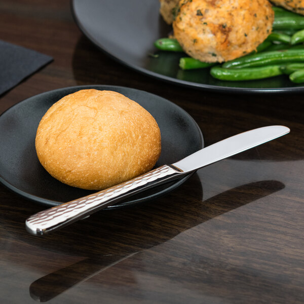 A black plate with food on it and a stainless steel bread and butter knife with a plain blade.