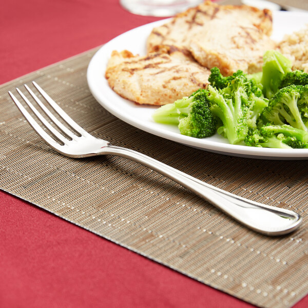 A Libbey stainless steel dinner fork next to a plate of broccoli and chicken.