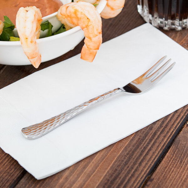A Libbey stainless steel cocktail fork on a white napkin with a bowl of shrimp.