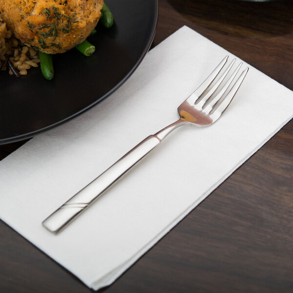 A Libbey Zephyr stainless steel salad fork on a napkin next to a plate of food.