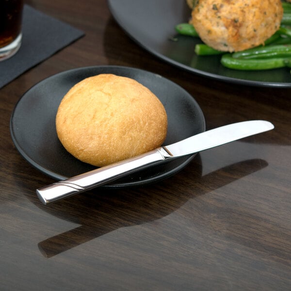 A Libbey stainless steel bread and butter knife on a plate with bread.