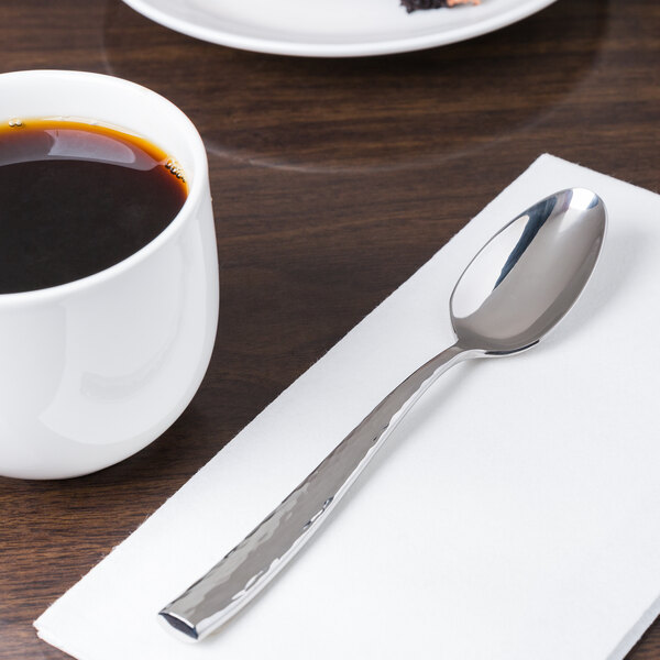 A Libbey stainless steel teaspoon on a napkin next to a cup of coffee.