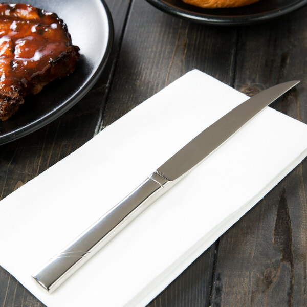 A Libbey Zephyr steak knife on a napkin next to a plate of food.