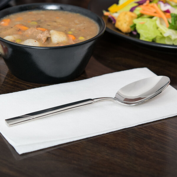 A Libbey stainless steel dessert spoon in a bowl of soup on a table.
