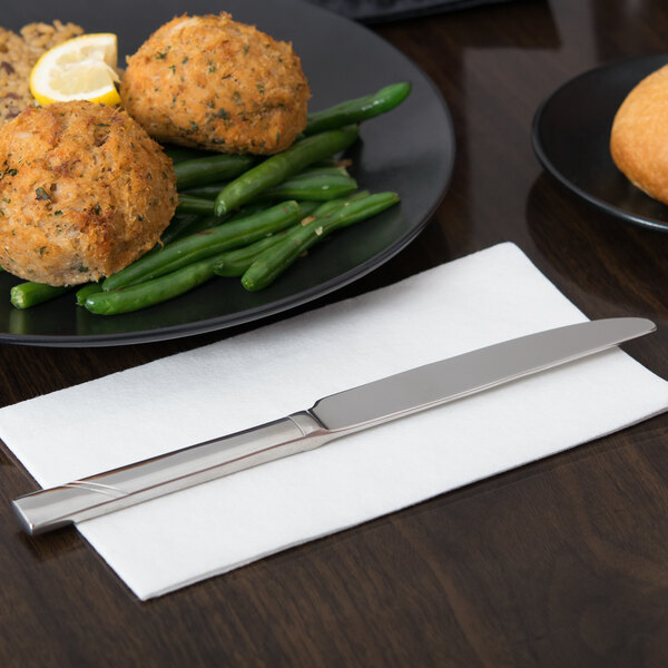 A Libbey stainless steel dinner knife on a white napkin next to a plate of food.