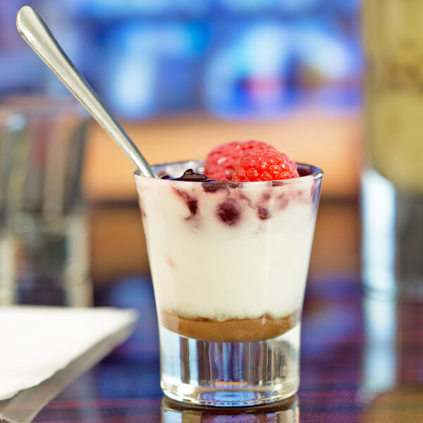 A Libbey shot glass with white liquid and a red berry on a spoon.