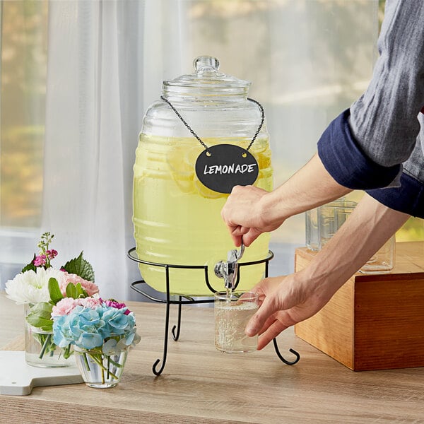 A person pouring lemonade from an Acopa barrel glass beverage dispenser.