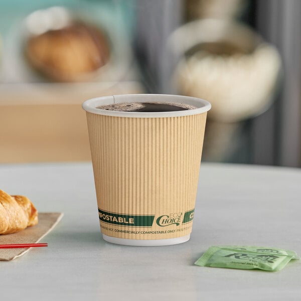 A close-up of an EcoChoice Double Wall Kraft Paper Hot Cup full of coffee on a table with a croissant.