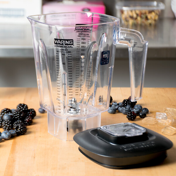 A Waring commercial blender with a clear blender jar filled with berries on a counter.
