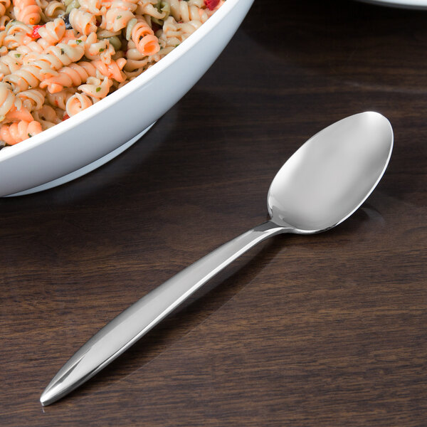 A Libbey extra heavy weight stainless steel serving spoon next to a bowl of pasta on a table.
