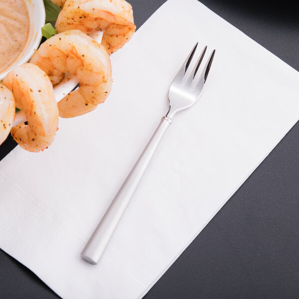 A Libbey stainless steel cocktail fork with shrimp on a white napkin.