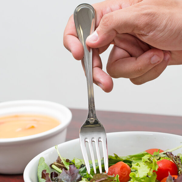 A hand holding a Libbey stainless steel salad fork over a bowl of salad.