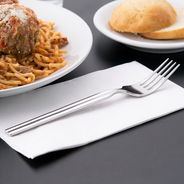 A fork on a napkin next to a plate of spaghetti and meatballs.