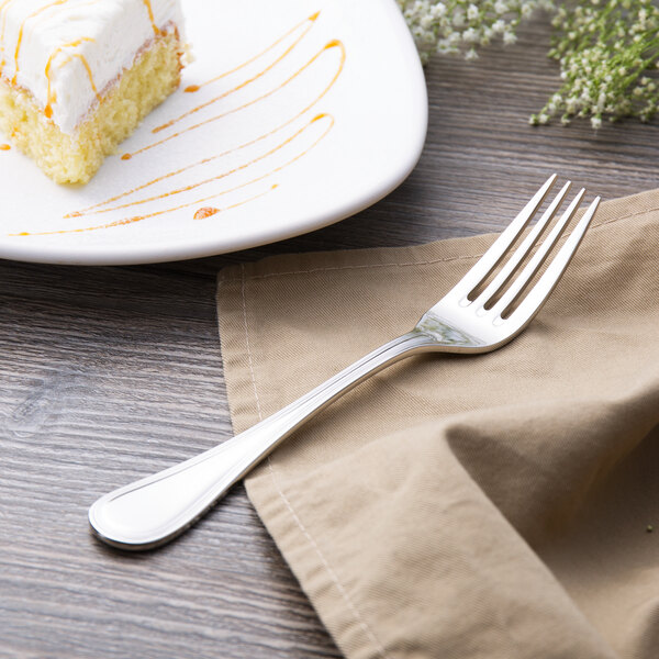 A Libbey stainless steel fork on a napkin next to a piece of cake.