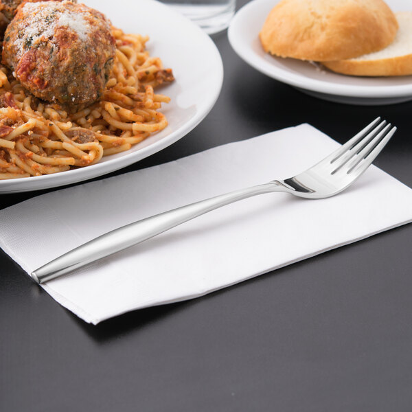 A Libbey stainless steel dinner fork on a napkin next to a plate of spaghetti and meatballs.