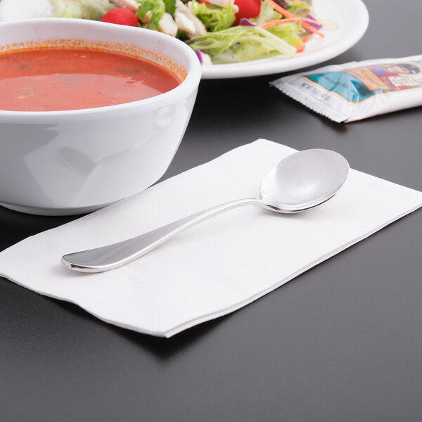 A bowl of soup and a Reserve by Libbey stainless steel bouillon spoon on a napkin.
