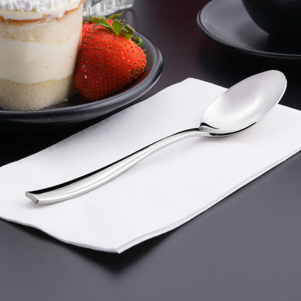 A Libbey stainless steel dessert spoon on a napkin next to a bowl of strawberries.