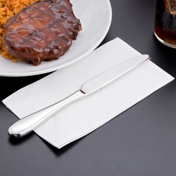 A plate of meat and rice with a Reserve by Libbey stainless steel dinner knife on a white napkin.