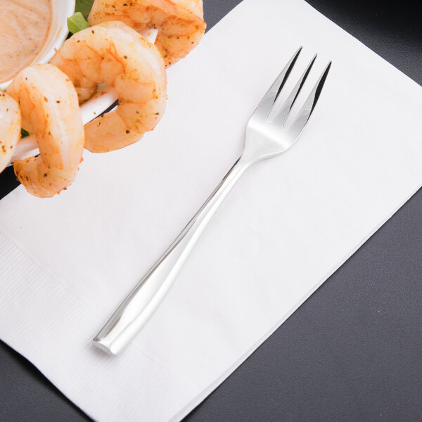 A Libbey stainless steel cocktail fork on a napkin with shrimp.