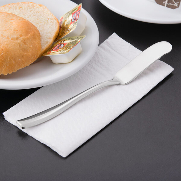 A plate with bread and a Libbey stainless steel butter spreader on a napkin.
