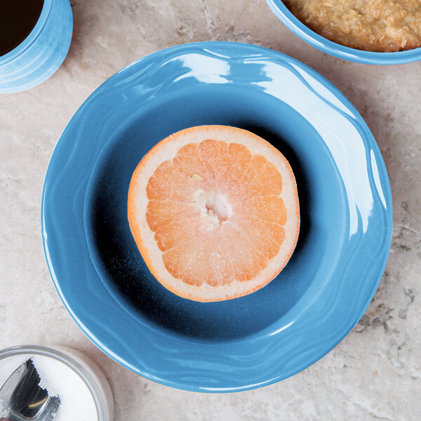 A blue Libbey porcelain bowl with a half of an orange next to a bowl of oatmeal.