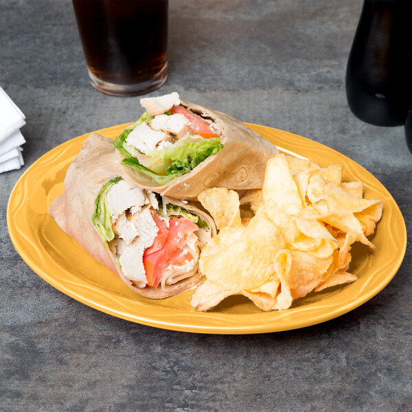 A sandwich and chips on a yellow Libbey Cantina porcelain platter on a table with a drink and napkins.